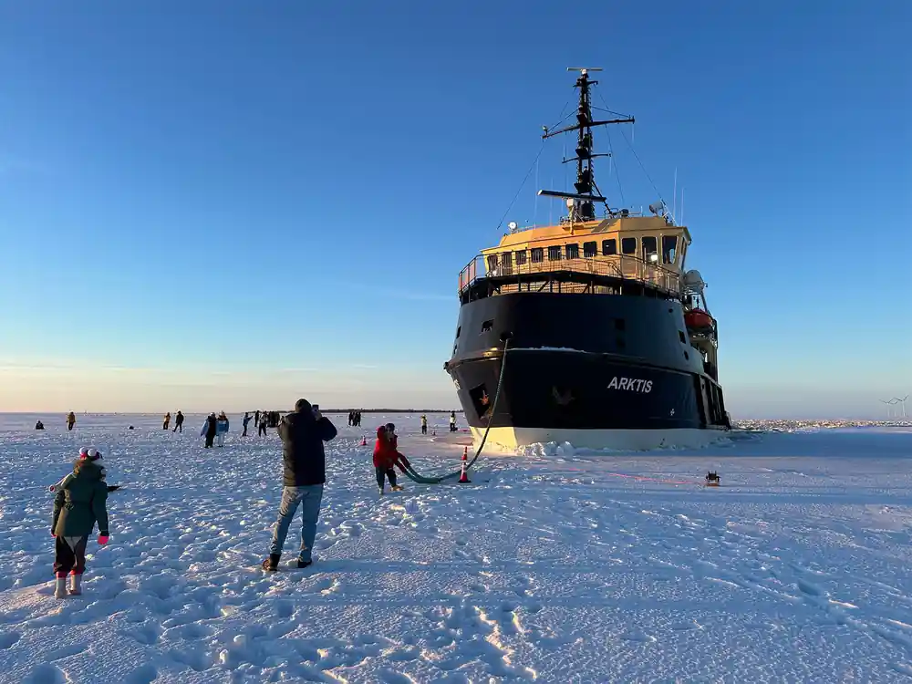 Arktis at rest on the ice with visitors walking towards the bow