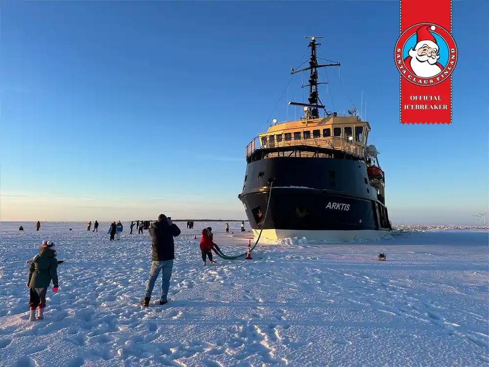 The bow of Arktis seen across the ice with visitors walking towards it