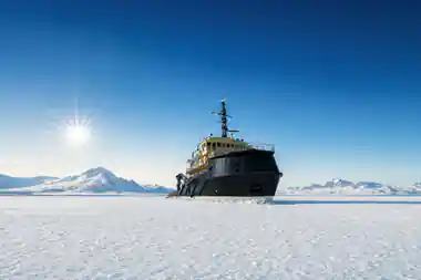 Icebreaker Arktis alongside an unbroken ice field under a clear blue sky