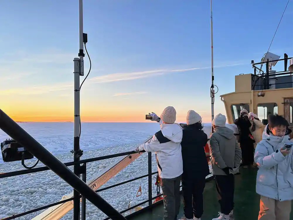 Passengers at the rail photographing a low sun over the ice