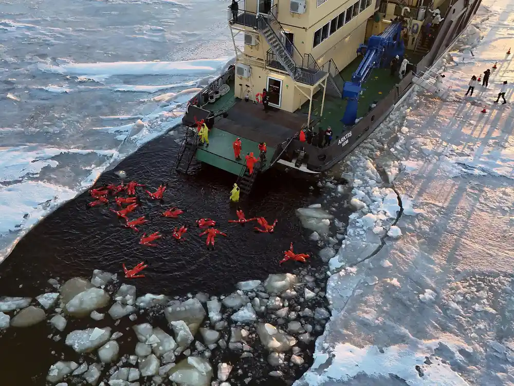 Passengers in the water in suits beside the ship stern ramp