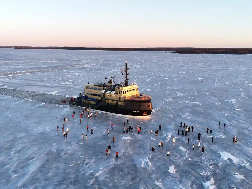 The ship in a broken channel with visitors on the surrounding ice