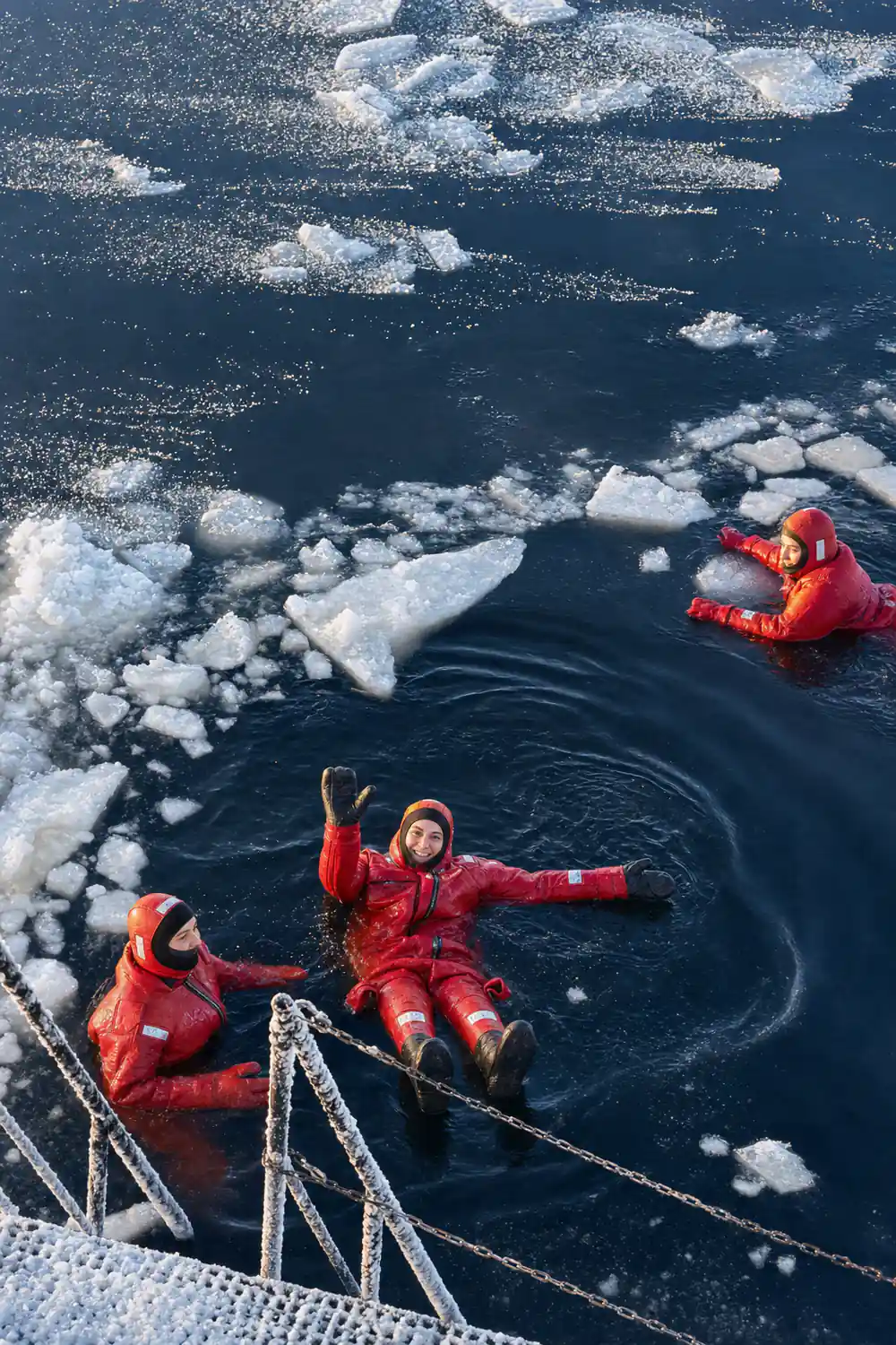 Two floaters in yellow suits in dark water among the ice