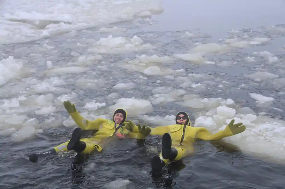 Two floaters in yellow suits lying back among the ice