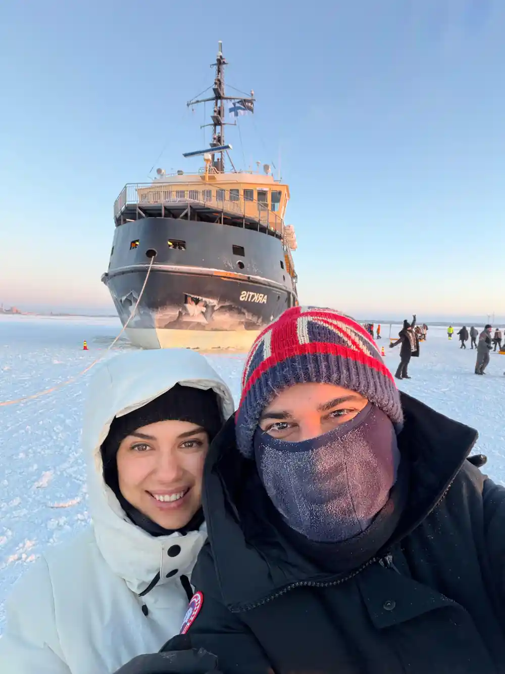Two visitors in hoods and a face covering with the ship behind them