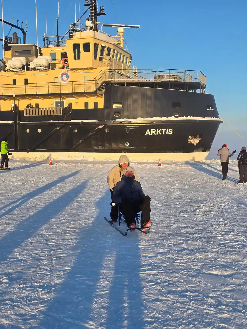 A visitor on a kicksled in front of the ship at sunset